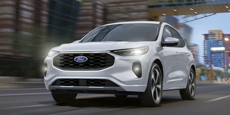 A white Ford Escape SUV driving on a city street at night